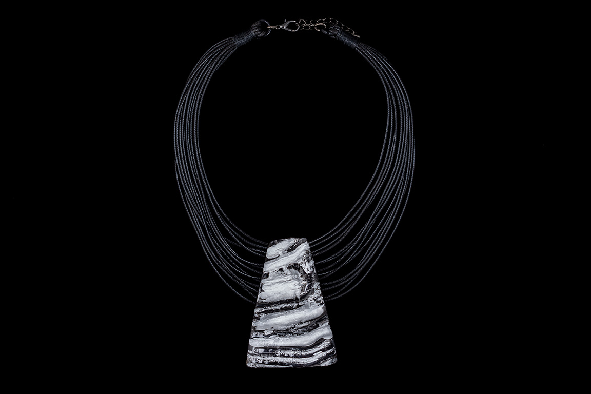 A Black Braided Leather Fourteen Strand Necklace With A Black And Silver Resin Grooved Triangular Pendant