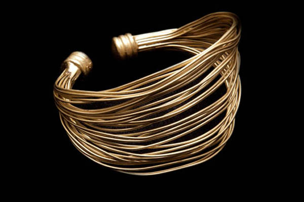 A Golden Metal Tapered Open Cuff With Curved And Curled Interlocking Bands