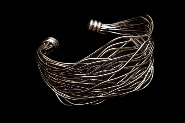 A Dark Silvered Metal Tapered Open Cuff With Curved And Curled Interlocking Bands