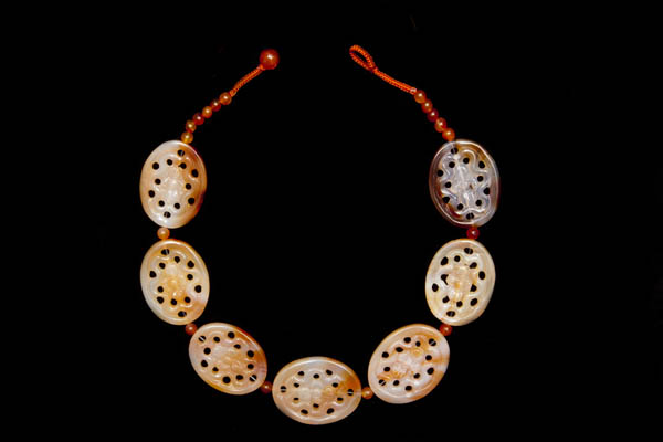 A Necklace Of Seven Chinese Light Orange Agate Carved And Pierced Floral Patterned Oval Beads