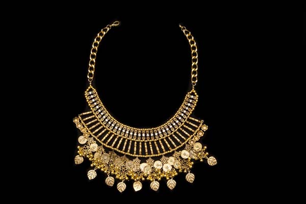 A Golden Metal Necklace With Two Bands Of Patterned Drops And Pendants Of Coins, Leaves, And Beads