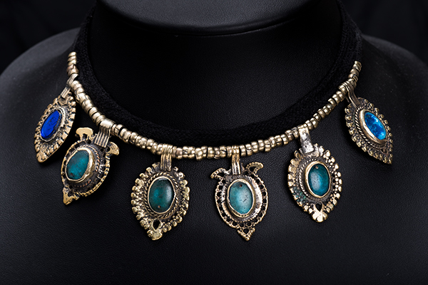 An Afghan Cloth Band Necklace With Six Silvered Metal Patterned Oval Drops With Blue Glass Insets