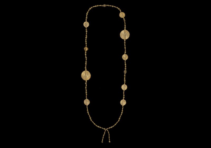 A Long Necklace Of Eight Akan Golden Metal Mixed Sized Patterned Discs, Three Baule Golden Metal Patterned Beads, And Eighty Ethiopian Small Mixed Shaped Brass Beads.