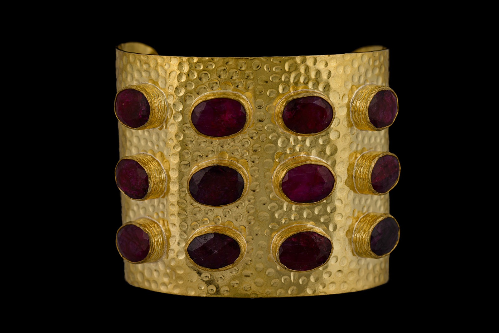 A Gold Plated, Hammered Surface, Open Cuff, Decorated With Twelve Ruby Facetted Oval Cabochons Set In Gold Plated Frames