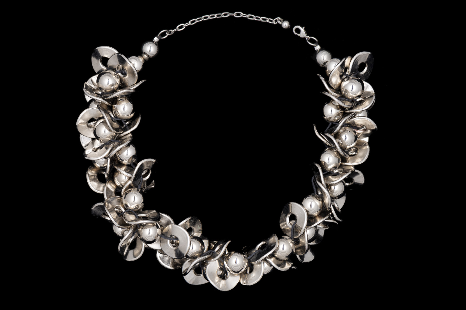 A Floral Patterned Necklace Of Thirty Five Silvered Metal Round Beads And Sixty-Five Silvered Metal Curved Discs.