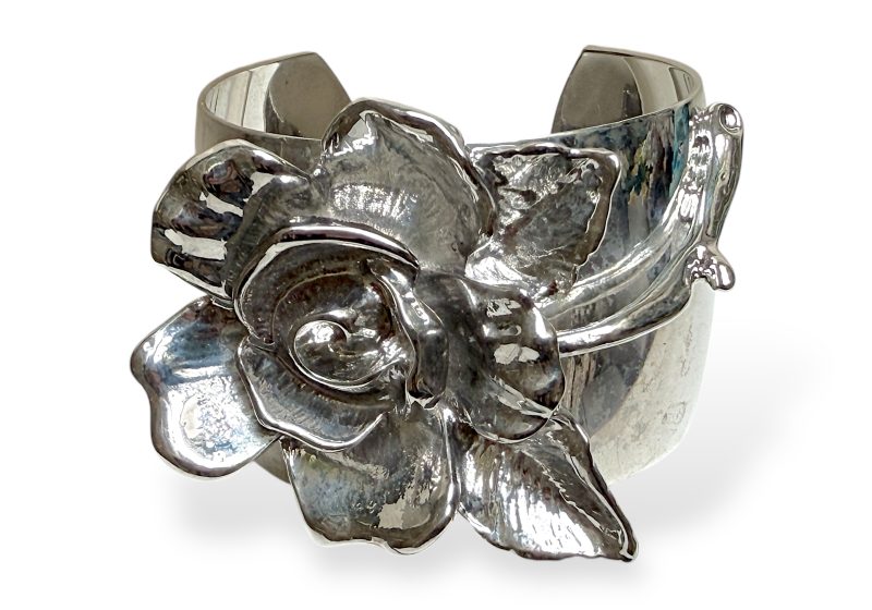 A Silvered Metal Wide Band Open Cuff With A Large Silvered Metal Ten Petalled Flower On A Stalk.
