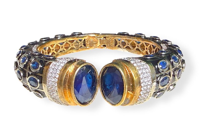 An Indian Gold Filled Hinged Bangle Decorated With Dark Blue And Clear Facetted Glass Cabochons