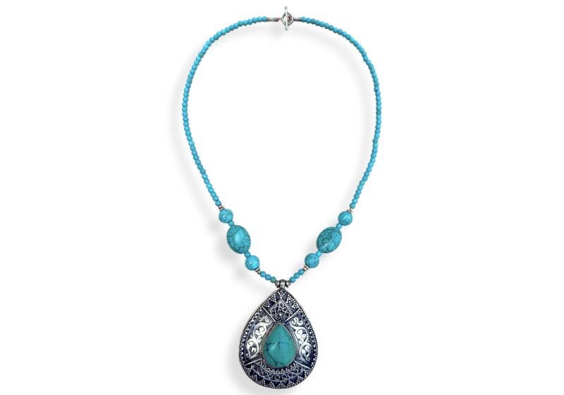 A Long Nepalese Necklace Of Turquoise Dyed Howlite Small Round Beads, With A Nepalese Silver Plated Patterned Teardrop Pendant Inlaid With A Turquoise Domed Teardrop Shaped Cabochon.