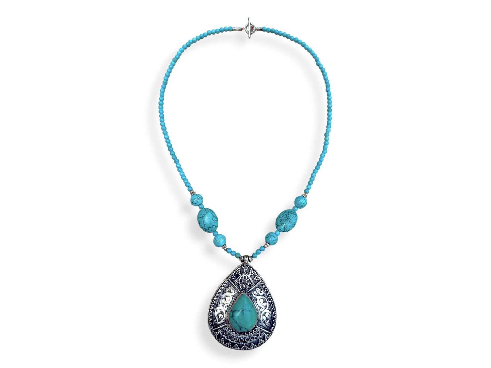 A Long Nepalese Necklace Of Turquoise Dyed Howlite Small Round Beads, With A Nepalese Silver Plated Patterned Teardrop Pendant Inlaid With A Turquoise Domed Teardrop Shaped Cabochon.