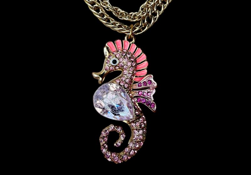 A Golden Metal Two Chains Long Necklace With A Seahorse Pendant Inlaid With Pink And Purple Facetted Glass Beads.